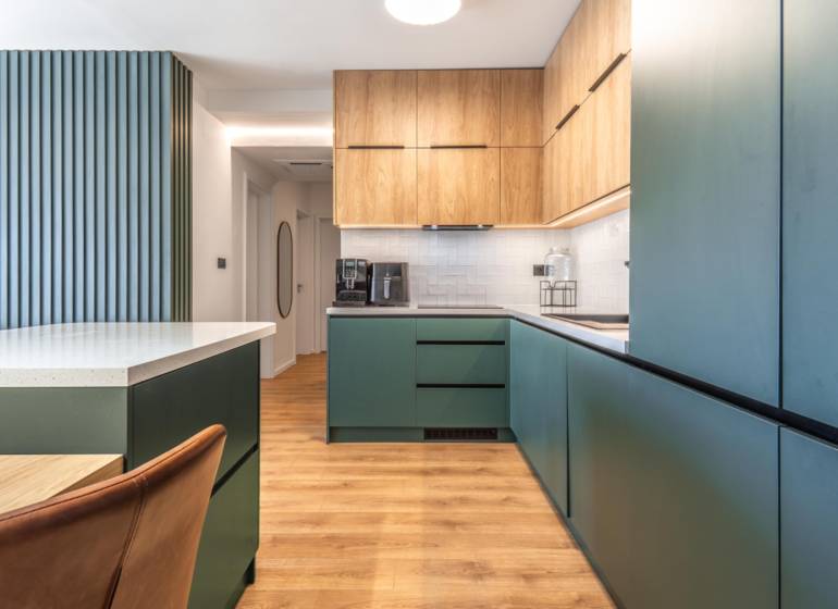 PRENÁJOM 3 izbový byt s predzáhradkou, BORY PROMENÁDA - Kuchyňa v 3-izbovom byte s podlahou s dreveným dekorom a zelenými skrinkami.