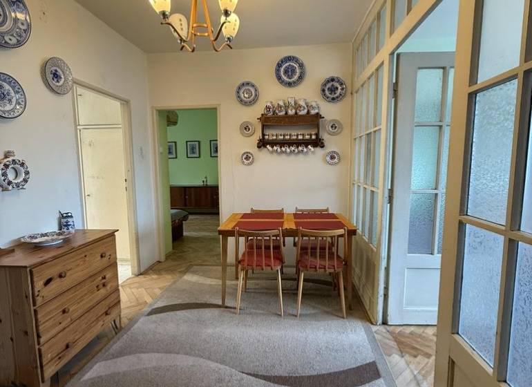 Novinka: Priestranný svetlý byt s balkónmi pri Kuchajde. Vajnorská - Jedáleň v 3-izbovom byte s dreveným dekorom, koberec, stôl a dekoratívne taniere.