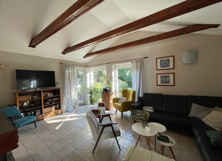 PREDAJ krásny 6 izb. rod. dom prepojený s prírodou - Obývacia izba s trámovým stropom, dlažbou, čiernou sedačkou a výhľadom do záhrady v rodinnom dome.