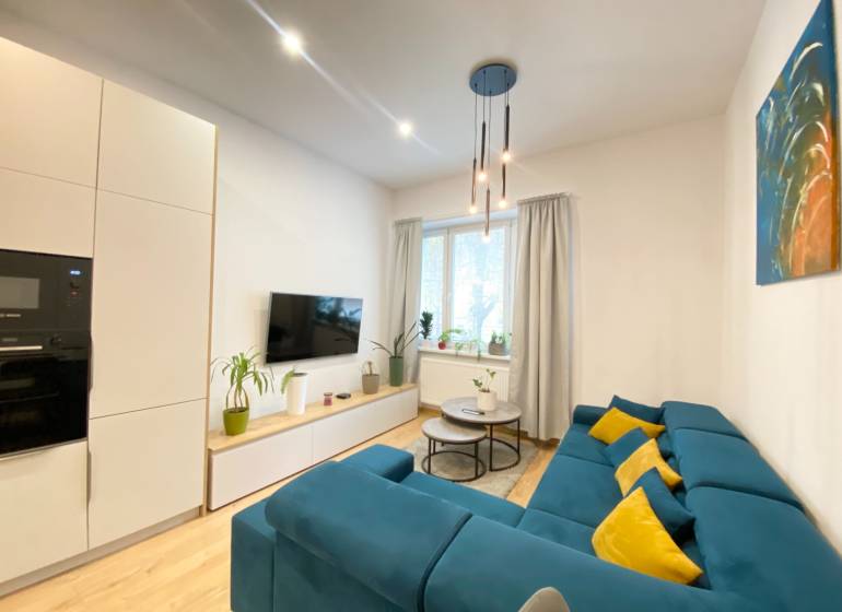 NA PRENÁJOM ŠTÝLOVÝ 2-IZBOVÝ BYT V CENTRE KOŠÍC, DREVNÝ TRH - Obývačka v 2-izbovom byte s modrou sedačkou a podlahou s dreveným dekorom.