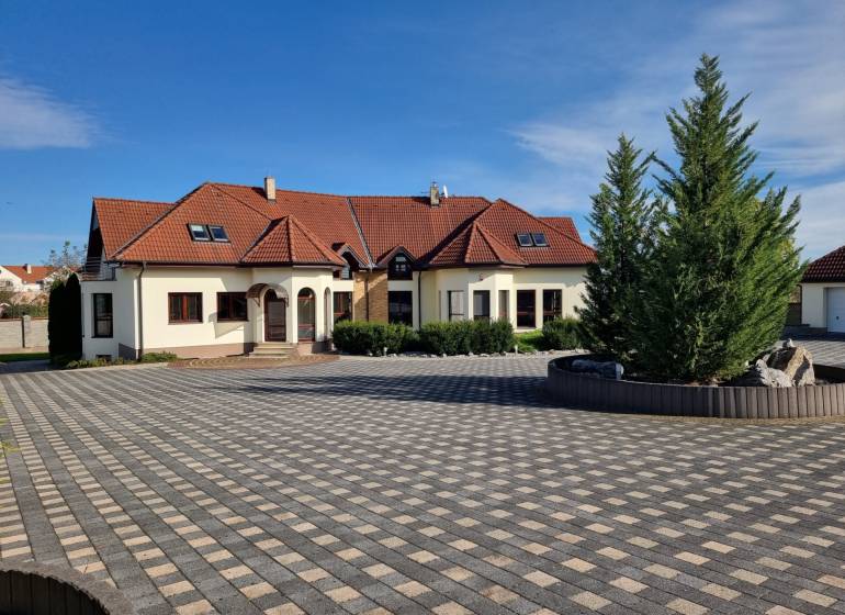 EXKLUZÍVNA VILA - NITRA - PREDAJ - Rodinný dom na Dolnočermánskej ulici v Nitre s veľkou dlaždenou plochou a stromami.