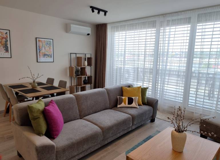 PRENÁJOM - 3 izbový byt Nitra – RIVIERA NITRA, Piesková ulica - Obývacia izba s pohovkou, jedálenským stolom a policami v 3-izbovom byte.