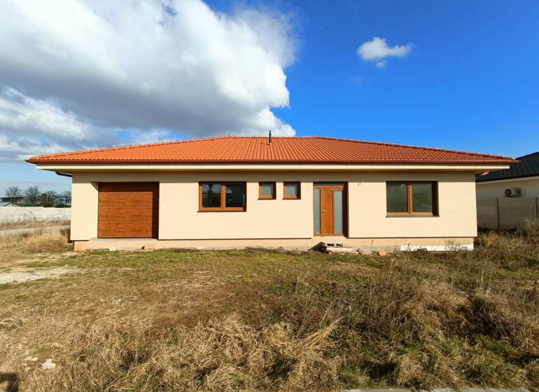 PREDAJ - 4 izbový holodom s veľkou garážou , Lužianky, Smreková ulica - Rodinný dom s červenou škridlovou strechou na trávnatom pozemku pod modrou oblohou.