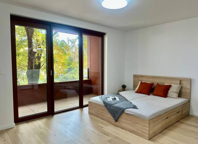 PRIESTRANNÝ 1-IZB. BYT S LOGGIOU V IKONICKOM PROJEKTE ZWIRN III - 1-izbový byt s veľkými oknami, podlaha s dreveným dekorom, balkón a posteľ.