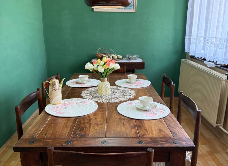 5-izbový rodinný dom v Borskom Mikuláši - bez rezervačej zálohy - Jedáleň v rodinnom dome s dreveným stolom, zelenou stenou a dekoráciami.