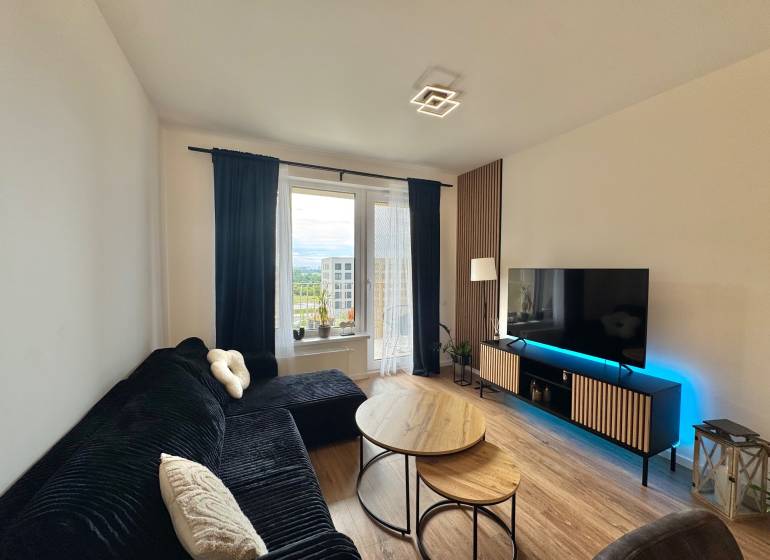 Nový 2-izbový byt na prenájom - Bory - Obývacia izba v 2-izbovom byte s čiernou sedačkou, stolíkmi a podlahou s dreveným dekorom.