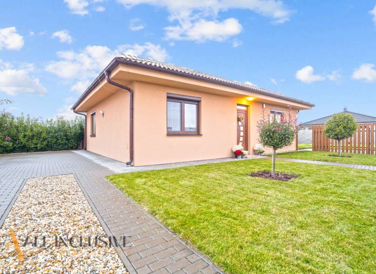 NA PREDAJ MODERNÝ 3-IZB. RD TYPU BUNGALOV V GABČÍKOVE - Rodinný dom v Gabčíkove obklopený zeleňou, dlažbou a malým stromčekom v záhrade.