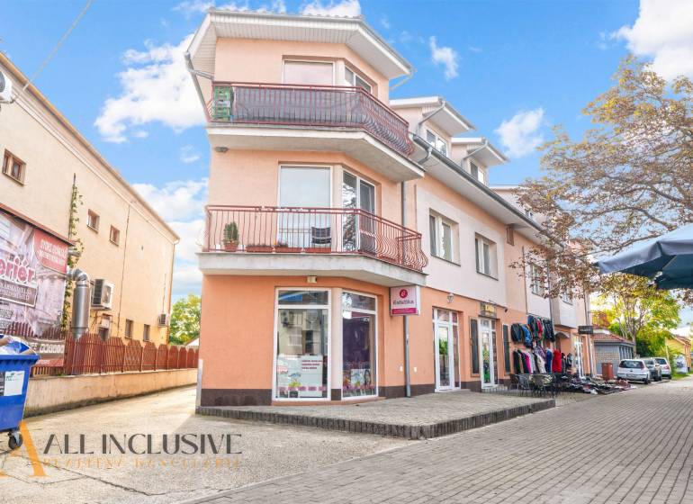 NA PREDAJ 2-IZBOVÝ BYT S 2 BALKÓNMI, DUNAJSKÁ STREDA - Budova na Kukučínovej ulici v Dunajskej Strede so svetlooranžovou fasádou a obchodmi.
