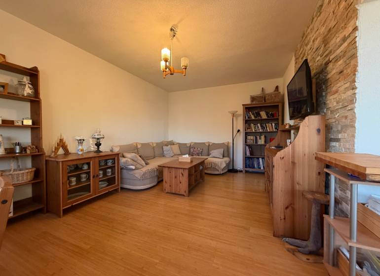 - PREDAJ - 2 izbový byt - Astrová ul. - Ružinov - Obývacia izba s pohovkou, podlaha s dreveným dekorom, knižnica a televízor na stene.