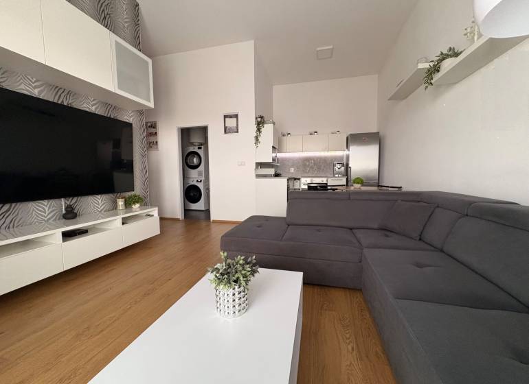 Prenájom moderného 2-izbového bytu v centre Komárna, 40 m² – Petőfiho  - Obývacia izba s veľkou sedačkou, podlahou s dreveným dekorom a televízorom v 2-izbovom byte.