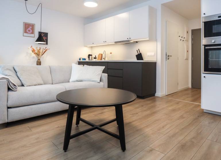 PRENÁJOM - 1 izbový byt v projekte Ovocné sady - Obývacia izba s kuchynským kútom v 1-izbovom byte, podlaha s dreveným dekorom.