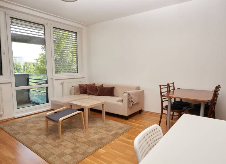 Ponúka prenájom 2 izb. byt na ul. Záporožská na začiatku - Obývacia izba s pohovkou, jedálenským stolom a podlahou s dreveným dekorom v 2-izbovom byte.