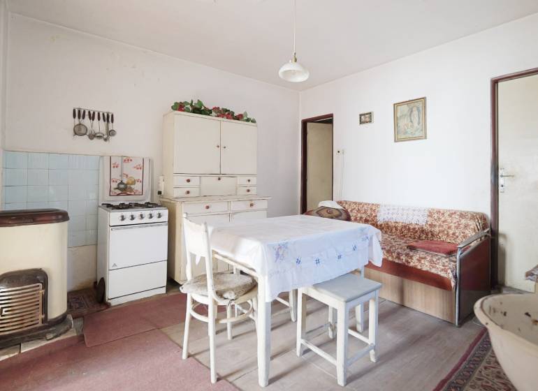 Menší rodinný dom len pár metrov od centra mesta Rajec - Jedáleň s plynovým sporákom, stolom a pohovkou v rodinnom dome, podlaha s dreveným dekorom.