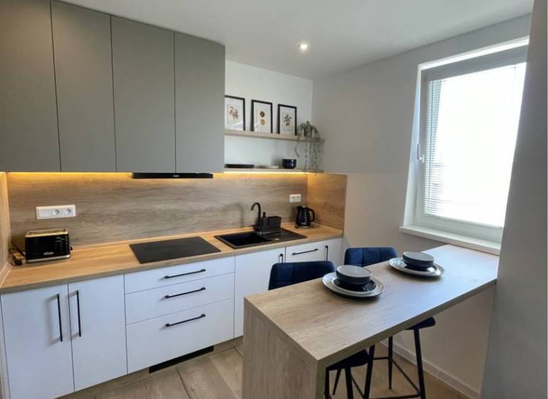 Vám ponúka na Prenájom 2-izbový byt s loggiou  - Kuchyňa v 2-izbovom byte s barovým pultom a podlahou s dreveným dekorom.