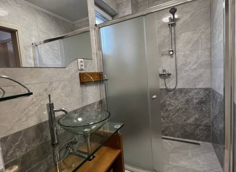 Vám ponúka na PREDAJ kompletne zrekonštruovaný  - Kúpeľňa v rodinnom dome s veľkým zrkadlom, skleným umývadlom a sprchovým kútom.