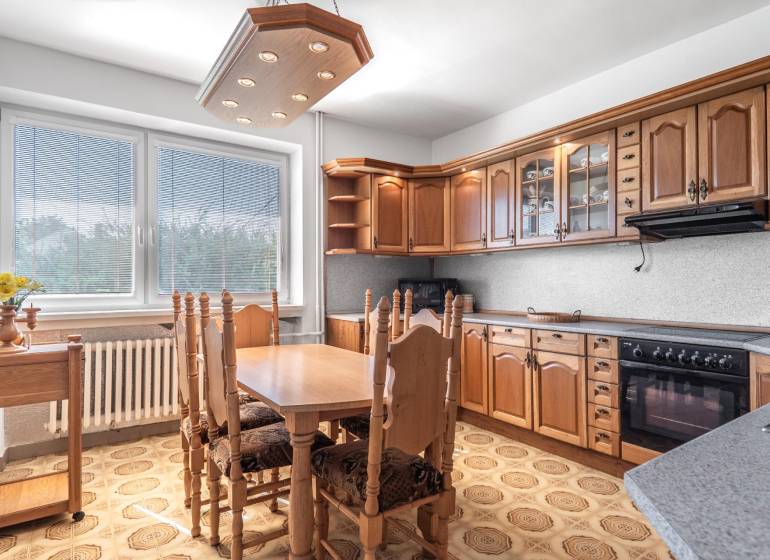 I Na predaj dvojposchodový 5i rodinný dom pri Žiline - Kuchyňa v rodinnom dome s drevenými skrinkami a jedálenským stolom, podlaha s dekorom.