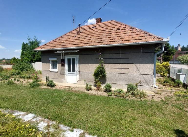 PREDAJ - ÚTULNÝ DOMČEK NA ROZĽAHLOM POZEMKU - NEVIDZANY - Rodinný dom v Nevidzanoch so záhradou, trávnikom a plotom, pod modrou oblohou.