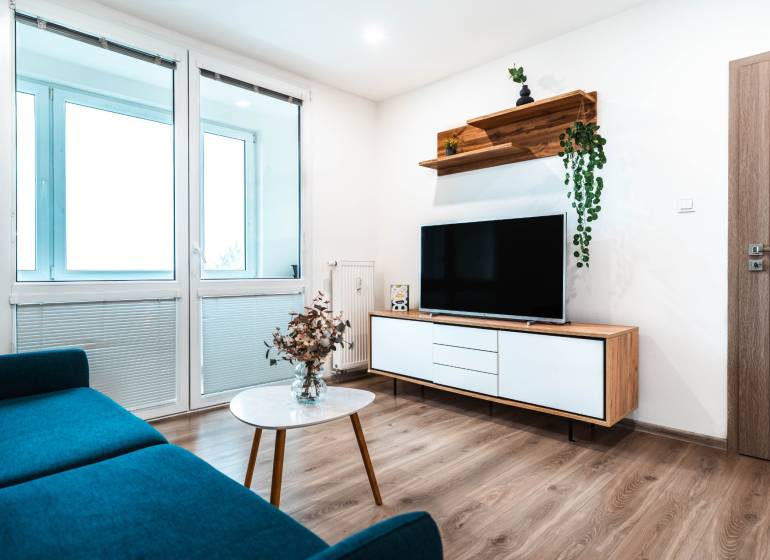 Útulný 2-izbový byt na prenájom - Obývacia izba v 2-izbovom byte so sedačkou, televízorom a podlahou s dreveným dekorom.