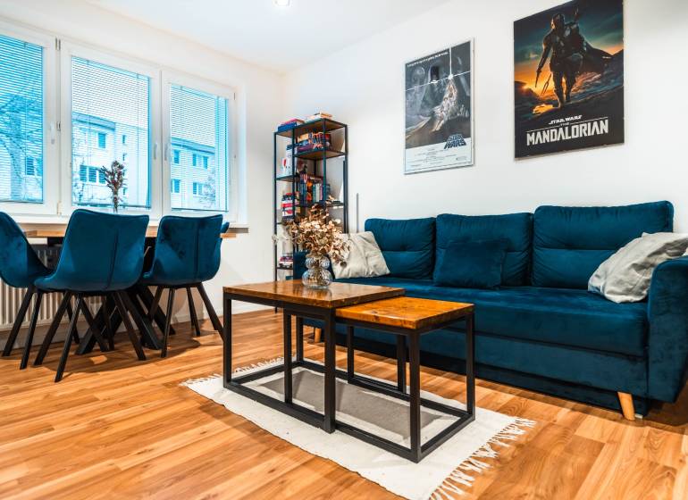 Na prenájom moderný 2-izbový byt  - Obývačka v 2-izbovom byte s modrou sedačkou a podlahou s dreveným dekorom.