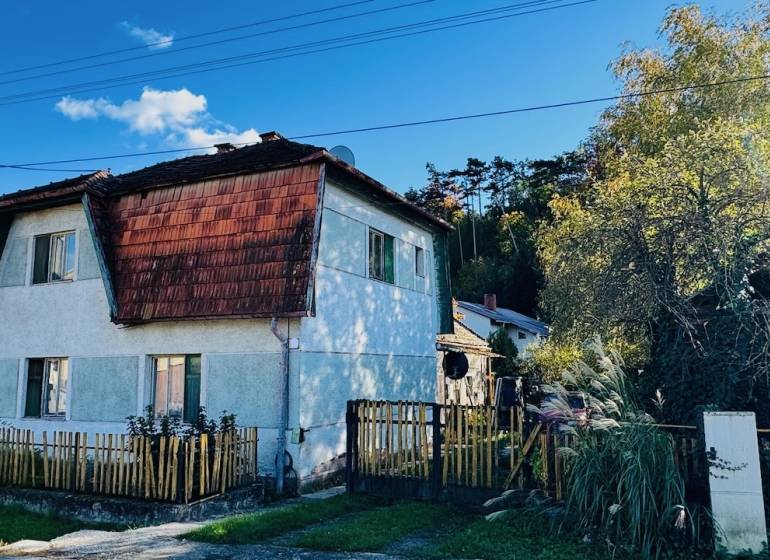 Na predaj 4-izbový rodinný dom v Brodzanoch – pozemok 1236 m² - Rodinný dom v Brodzanoch s dreveným plotom a šikmou strechou, obklopený zeleňou.