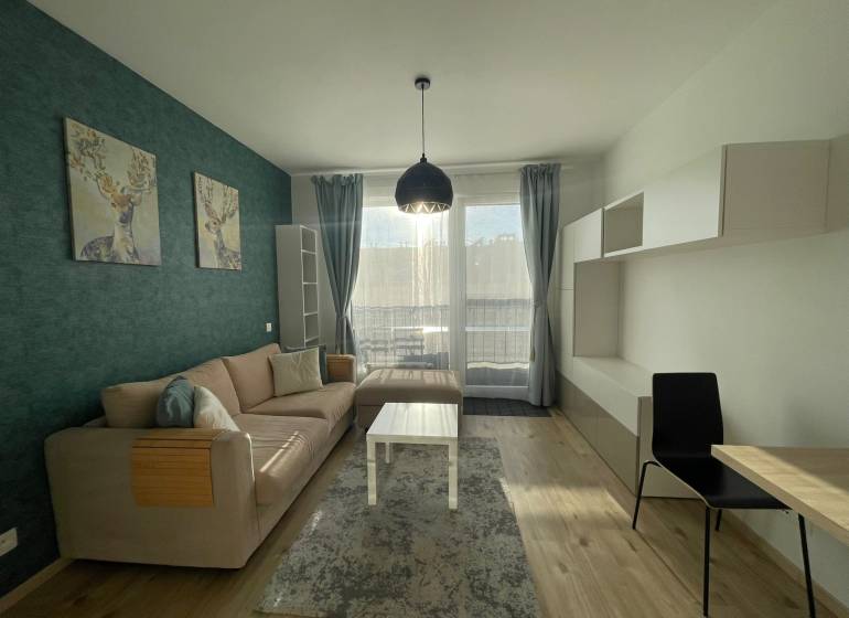 MODERNÝ, KOMPLETNE ZARIADENÝ 1-IZBOVÝ BYT V PROJEKTE SLNEČNICE - Obývačka 1-izbového bytu s pohovkou, dekoráciou jeleňa a podlahou s dreveným dekorom.