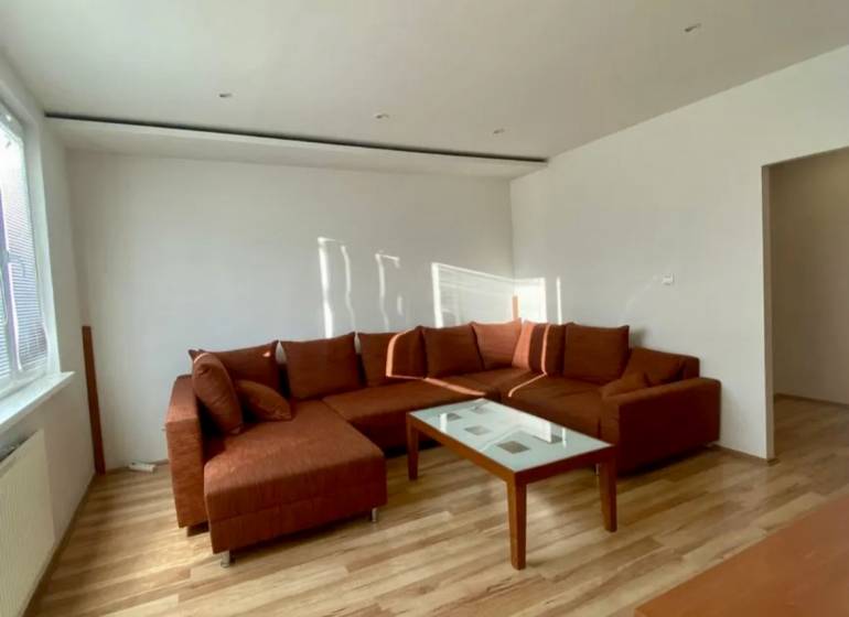 Pekný 3 izbový byt s lodžiou, ulica Nad Lúčkami, BA IV. Karlova Ves - Obývačka v 3-izbovom byte s rohovou sedačkou, stôl a podlaha s dreveným dekorom.