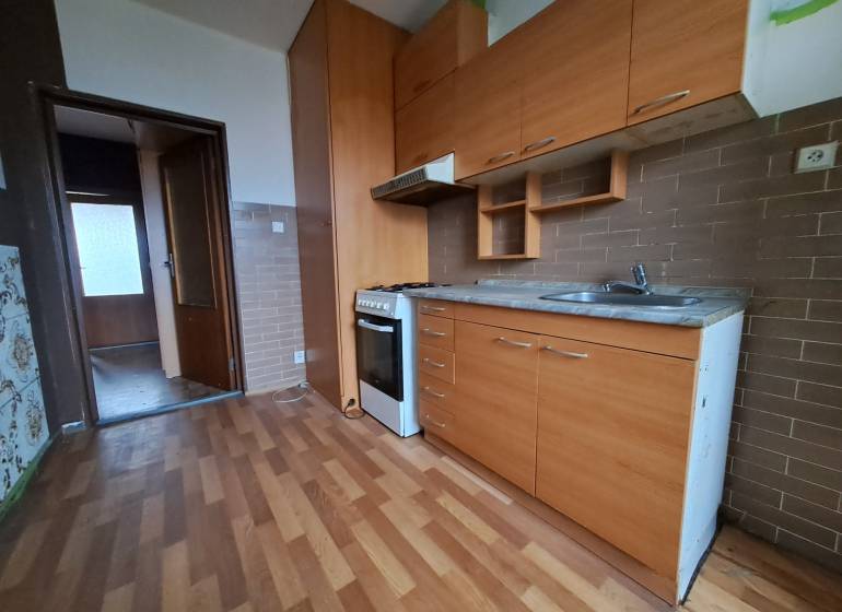 REZERVOVANÉ 2-izbový byt s nádherným výhľadom v pôvodnom stave   - Kuchyňa s kuchynskou linkou a spotrebičmi v 2-izbovom byte na podlahe s dreveným dekorom.