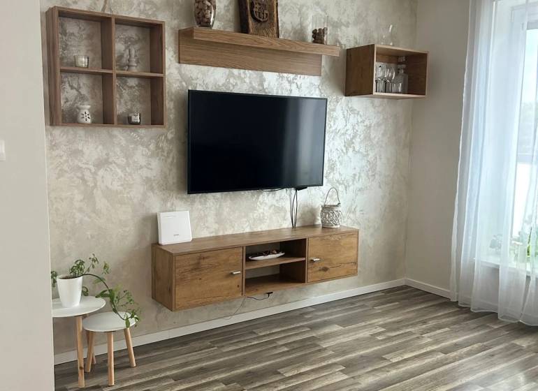 Praktický 3-izbový byt v súkromnej ulici v Šamoríne - Obývačka v 3-izbovom byte s podlahou s dreveným dekorom, zavesenou TV a dekoráciami.