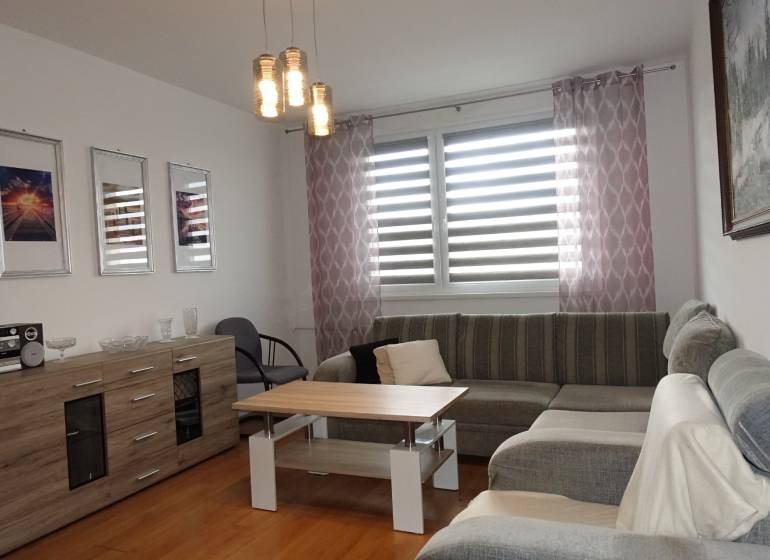 PREDAJ- 3-iz. byt, Homolova - Dúbravka, 67 m2, 11./12. posch., lodžia - Svetlá obývačka s rohovou sedačkou, stolíkom a komodou v 3-izbovom byte.