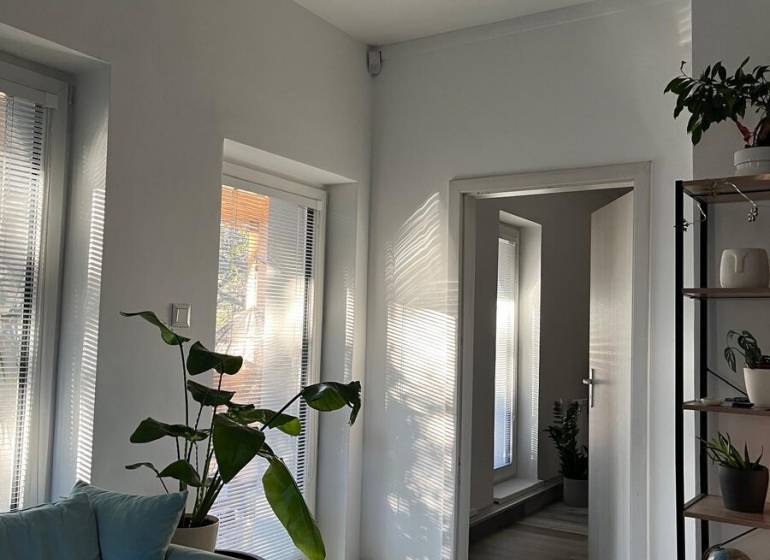 Na predaj moderný 4-izbový byt s veľkou terasou a súkromnou záhradou - Svetlá obývacia izba s rastlinami, sedačkou a podlahou s dreveným dekorom v 4-izbovom byte.