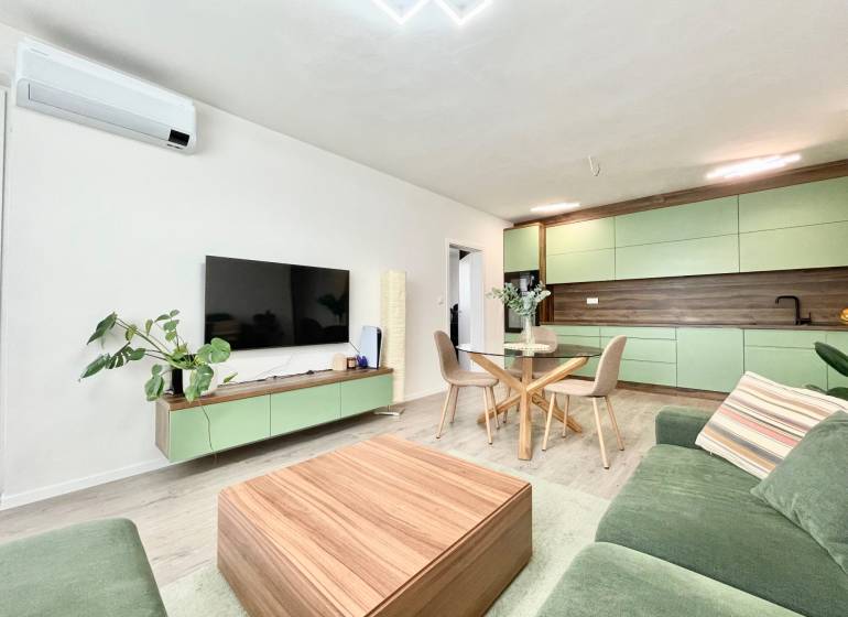 Na predaj štýlový 2-izbový byt s loggiou a parkovaním – TN, Na Pažiti - Obývacia izba v 2-izbovom byte s kuchyňou a podlahou s dreveným dekorom.