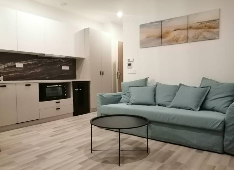 ŠIKOVNÁ GARSÓNKA na PRENÁJOM v CENTRE MESTA na BEZRUČOVEJ ul. - Garsónka s kuchyňou, modrým gaučom, okrúhlym stolíkom a podlahou s dreveným dekorom.