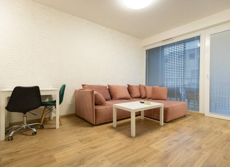 Zariadený 2i byt s lodžiou v rezidencii Pri Mýte - Obývacia izba v 2-izbovom byte s pohovkou, stolom a podlahou s dreveným dekorom.