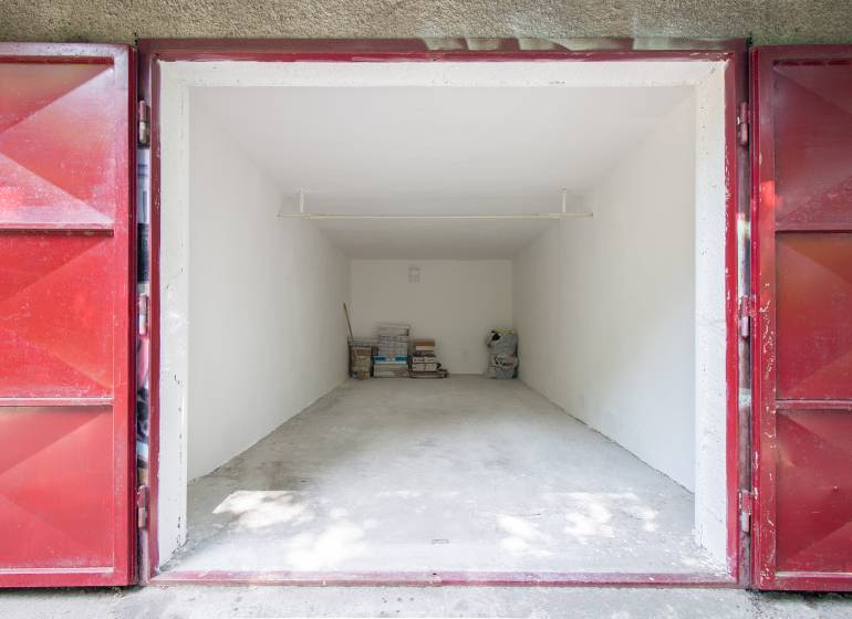 Pozrite si 17m², ZREKONŠTRUOVANÚ garáž, pri nemocnici Kramáre - Otvorená garáž so skladovanými predmetmi na ulici Opavská a Garáže, červené dvere.