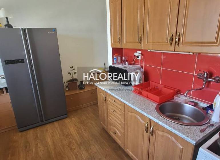 Predaj, jednoizbový byt Žiar nad Hronom, Novomeského - Kuchyňa v 1-izbovom byte s drevenými skrinkami, červenými kachličkami a veľkou chladničkou.