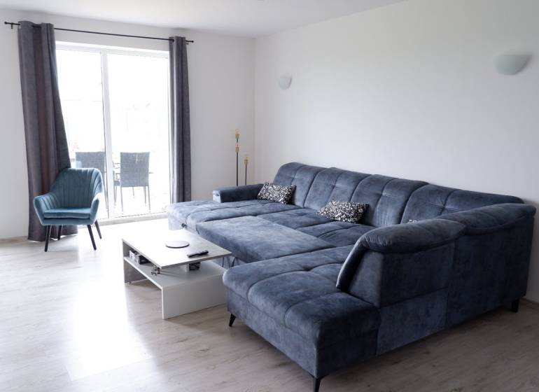 Ponúkame na predaj 3 izbový radový dom v obci Rastislavice. - Obývacia izba s modrou sedacou súpravou a kreslom, podlaha s dreveným dekorom, Rodinný dom.