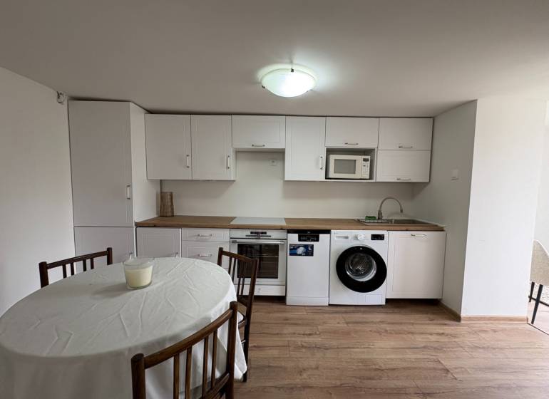 NA PRENÁJOM krásny 1 izbový apartmán so záhradou v srdci Komárna - Kuchyňa v 1-izbovom byte s bielymi skrinkami a podlahou s dreveným dekorom.