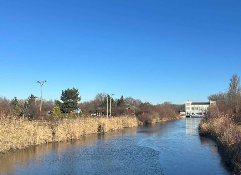 PREDAJ : ZÁHRADA S MUROVANOU CHATKOU, KOMÁRNO - Rieka obklopená rákosím v Záhradách na Novej osade v Komárne pod modrou oblohou.