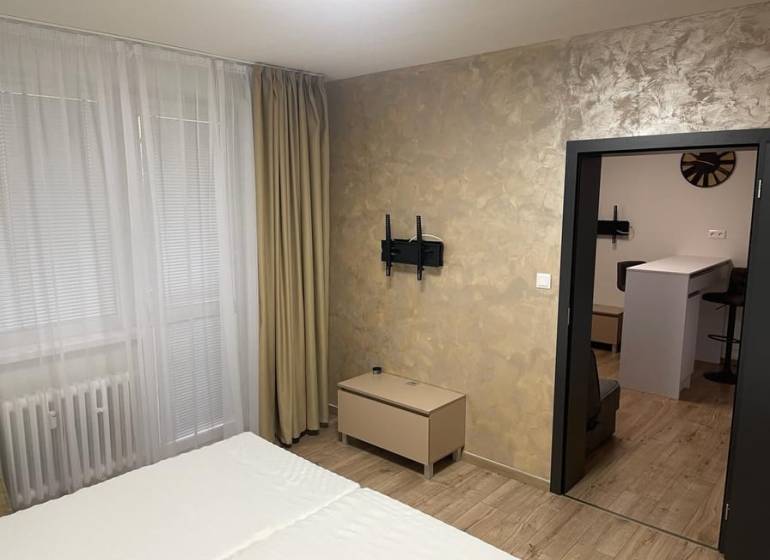 REZERVOVANÉ! Nadštandardný 1-izbový byt, ul. 1. mája, Vráble - Interiér 1-izbového bytu s podlahou s dreveným dekorom, postele a závesy na okne.