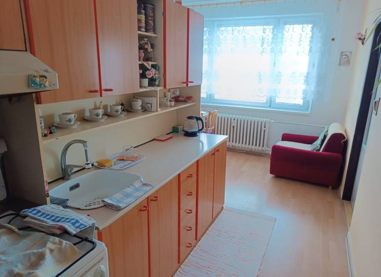 Na predaj veľkometrážny 3 izbový byt Žarnovica - Kuchyňa v 3-izbovom byte s podlahou s dreveným dekorom, vybavená skriňami a pohovkou.