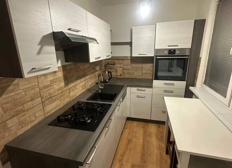 2-izb. byt, Nejedlého, Dúbravka, izby samostatné - Kuchyňa v 2-izbovom byte s podlahou s dreveným dekorom a stenami z tehál.