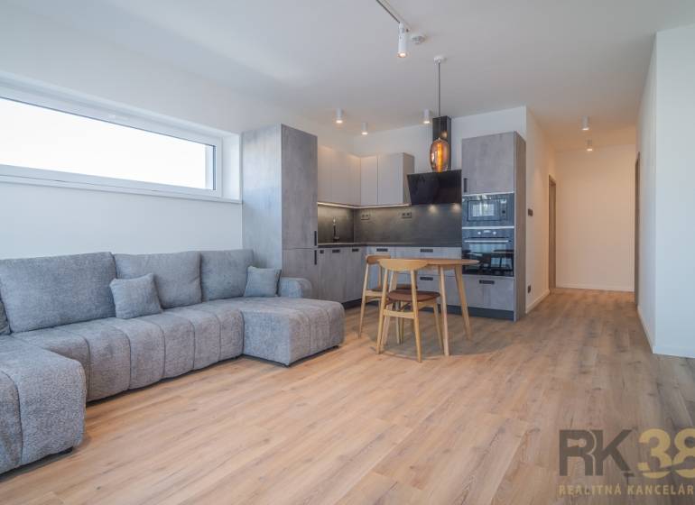 Na prenájom lukratívne 2-izbové byty v centre Popradu - Obývacia izba v 2-izbovom byte so sivou sedačkou a kuchyňou s dreveným nábytkom.