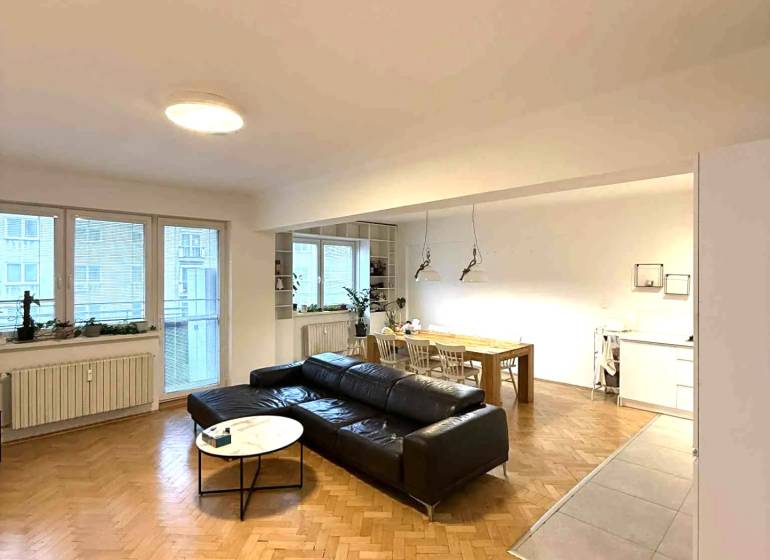 Prenájom 4 izb. bytu, Blumentálska ulica, Staré Mesto - Obývacia izba v 4-izbovom byte s podlahou s dreveným dekorom a čiernym gaučom.