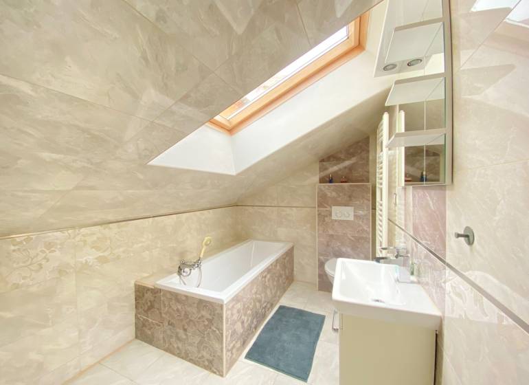 KRÁSNY DVOJPODLAŽNÝ RODINNÝ DOM NA PRENÁJOM - Kúpeľňa v rodinnom dome s vaňou, oknom v streche a svetlými obkladmi.