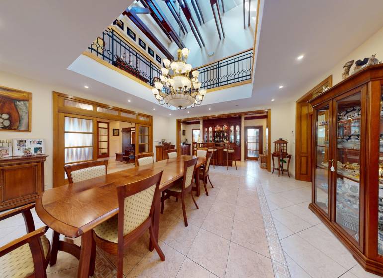 Veľkometrážny dom s wellness, bazénom a investičným potenciálom - Jedáleň v rodinnom dome s veľkým dreveným stolom, lustrom a vitrínami s porcelánom.