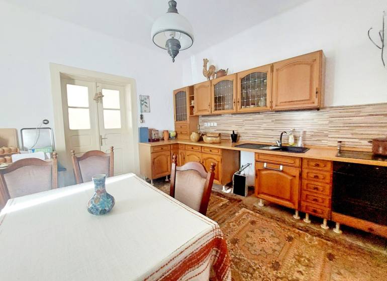 NA PREDAJ rodinný dom - Lehota nad Rimavicou - Kuchyňa v rodinnom dome s dreveným nábytkom, stolom a dekoračnou vázou.