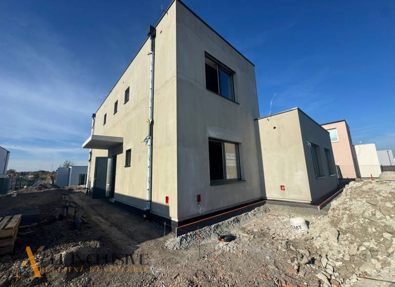 NA PREDAJ 4-IZB. POSCHODOVÝ RD (ČASŤ DVOJDOMU), HUBICE - Rodinný dom v Hubiciach vo výstavbe, s minimalistickým exteriérom a susednými budovami.