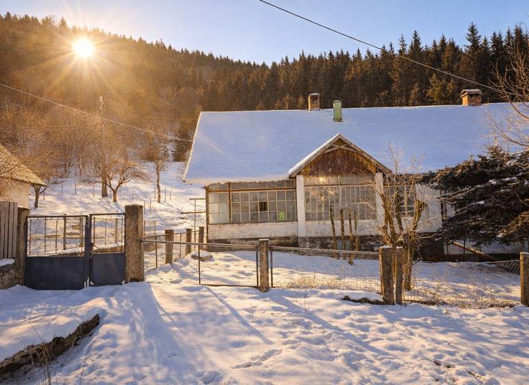 Predaj, rodinný dom Sliačany, Donovaly - Zasnežený rodinný dom v Donovaloch, obklopený stromami a zachytený pod zapadajúcim slnkom.
