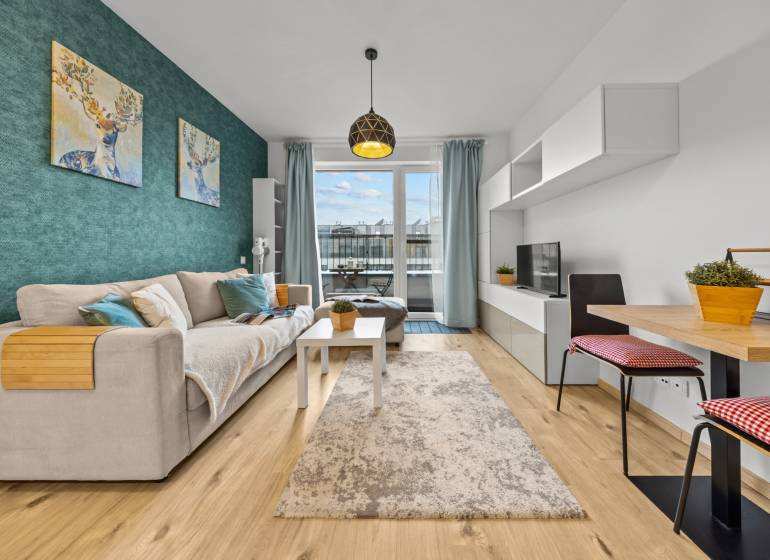 ZARIADENÝ 1-IZBOVÝ BYT, SLNEČNICE – IDEÁLNA INVESTÍCIA AJ BÝVANIE - Obývacia izba v 1-izbovom byte s pohovkou, TV, kobercom a podlahou s dreveným dekorom.