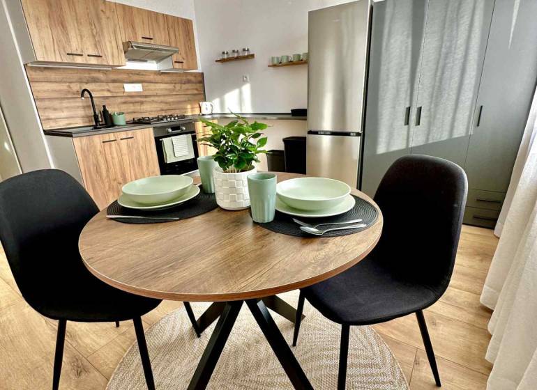 REZERVOVANÝ PREDAJ 1-izbový byt, Vlčince - okr. Žilina - Kuchynský kút v 1-izbovom byte s dreveným dekorom a kruhovým stolom.